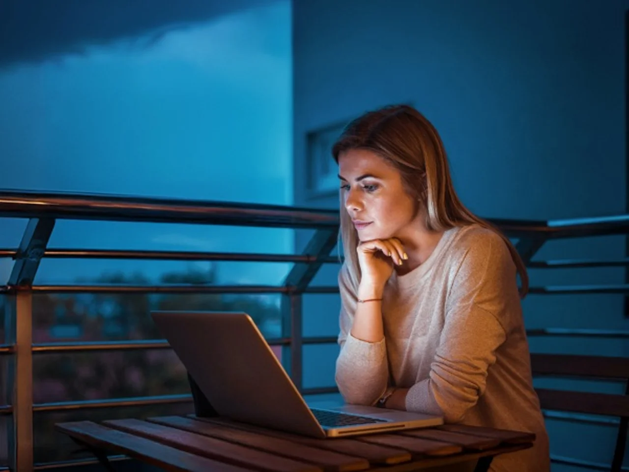 Person seated at a terrace table using a laptop after sunset.