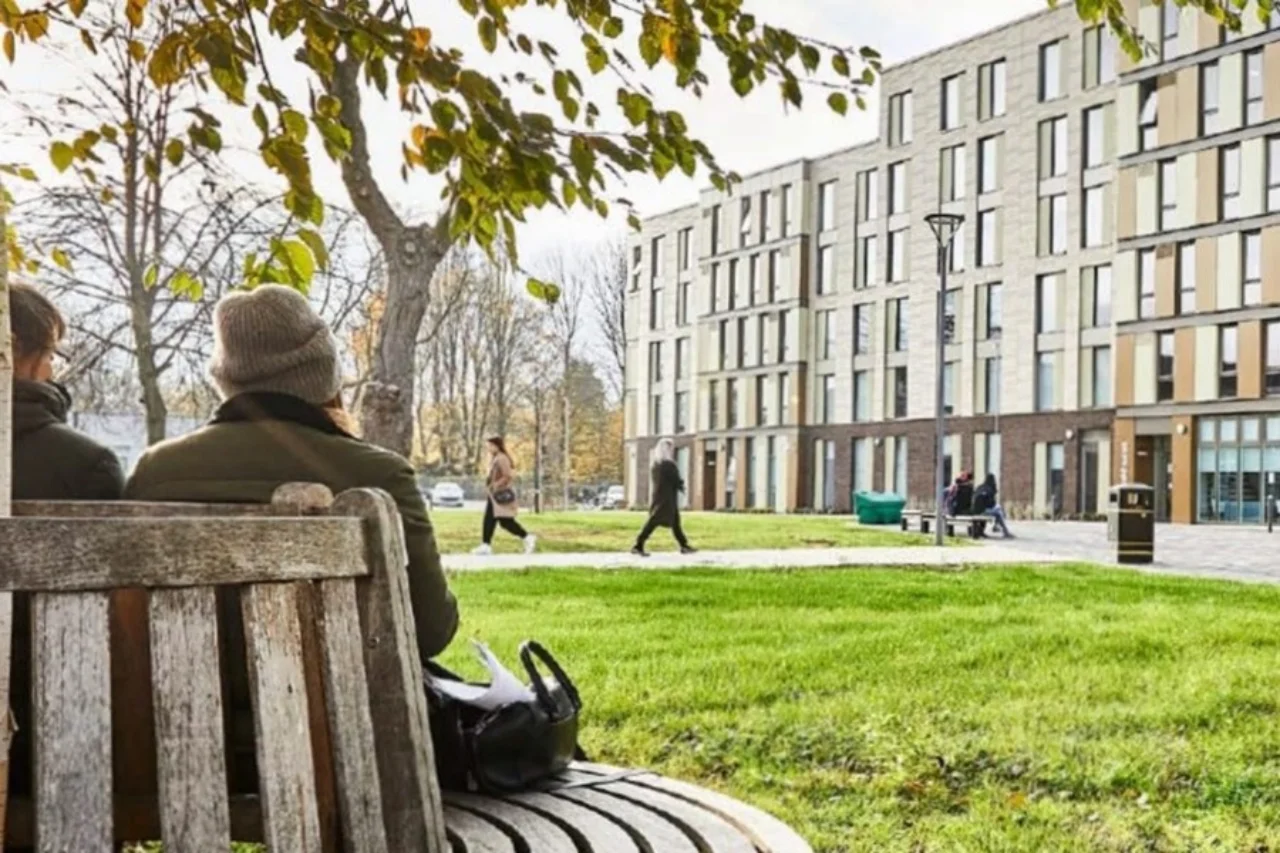 Two people relax on a wooden bench in a park.